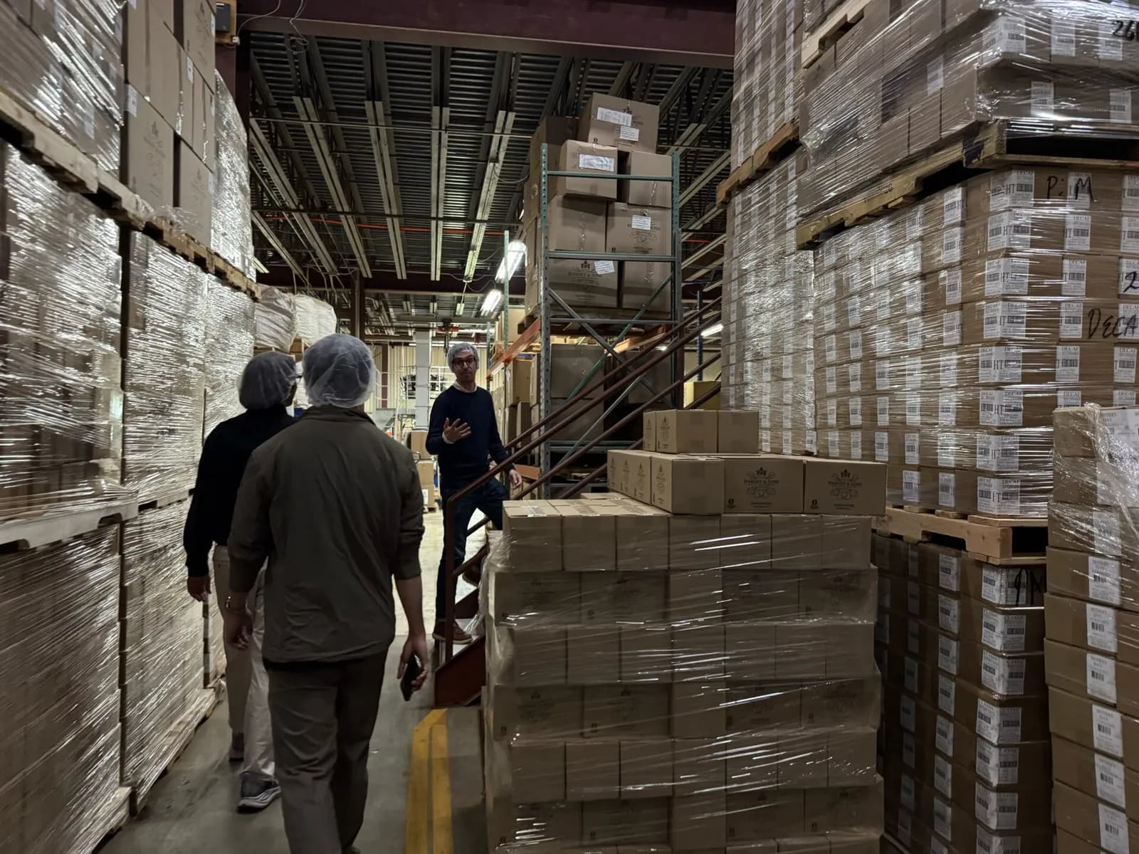 Structify team members in hairnets touring a client's warehouse between stacked pallets